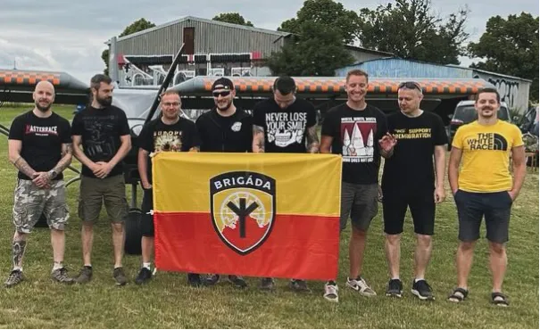 Jen pár měsíců stará fotka z posezení Brigády u letiště ve Vyškově, kterého se zúčastnil i Pavel Kamas a několik aktivistů Nacionalistů. Zcela vlevo stojí Ondřej Loužecký ve svém oblíbeném tričku, za vlajkou je s obrácenou kšiltovkou Martin Loužecký a vedle něj s trikem NLYS Vítězslav Baránek. Vpravo v triku “The White Race” Jakub Svoboda.