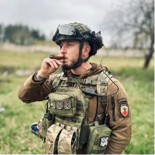 Marťák Loužecký se velmi rád fotí v military gearu. Tady má sumku s čísly 1488. Číslice 14 odkazuje na tzv. 14 slov, která formuloval americký neonacista David Lane: „Musíme chránit naše lidi a budoucnost našich dětí,“ číslo 88 pak vyjadřuje Heil Hitler (podle pořadí písmen v abecedě). Heslo Never Lose Your Smile (NLYS), které má na nášivce na boční sumce, je oblíbený neonacistický internetový mem odkazující k výrazu tváře Totenkopfu, lebky ze znaku jednotek SS. Na fotografii je vidět také nášivka skupiny Brigáda se symbolem černého slunce v pozadí a runou Algiz, “runou života” (Lebens-Rune), dalším z motivů populárních mezi neonacisty.  